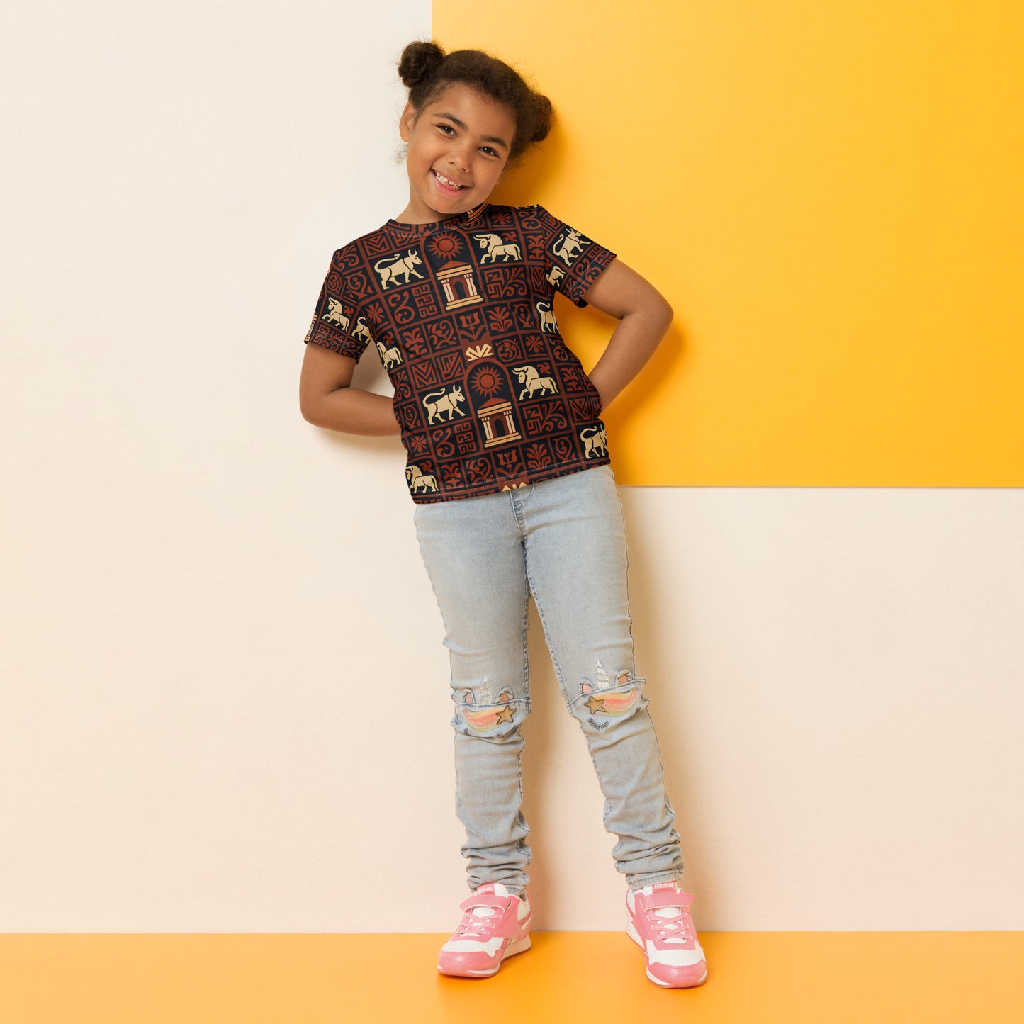 Young girl wearing a patterned shirt and light blue jeans against a yellow and beige background