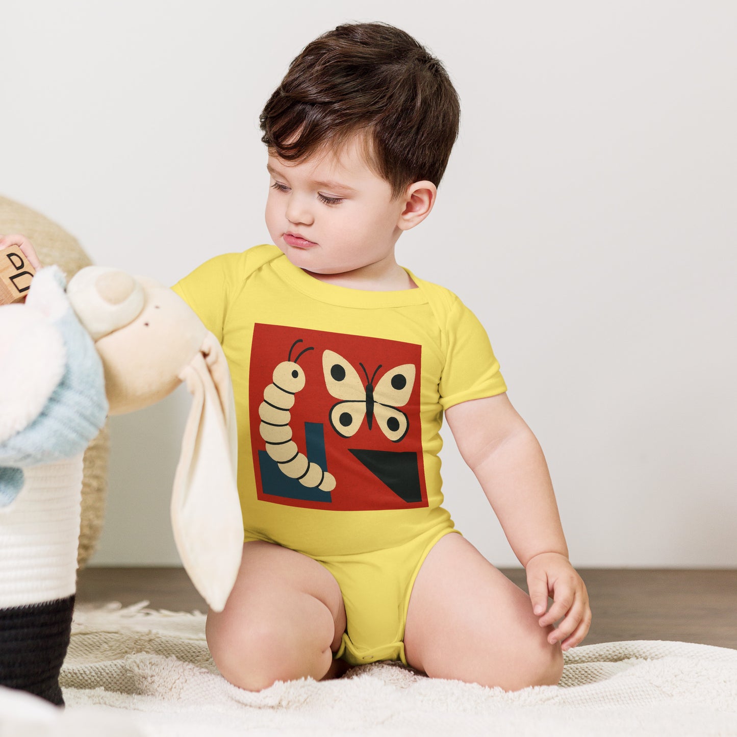 Child wearing a yellow onesie with a butterfly design, sitting on a white blanket.