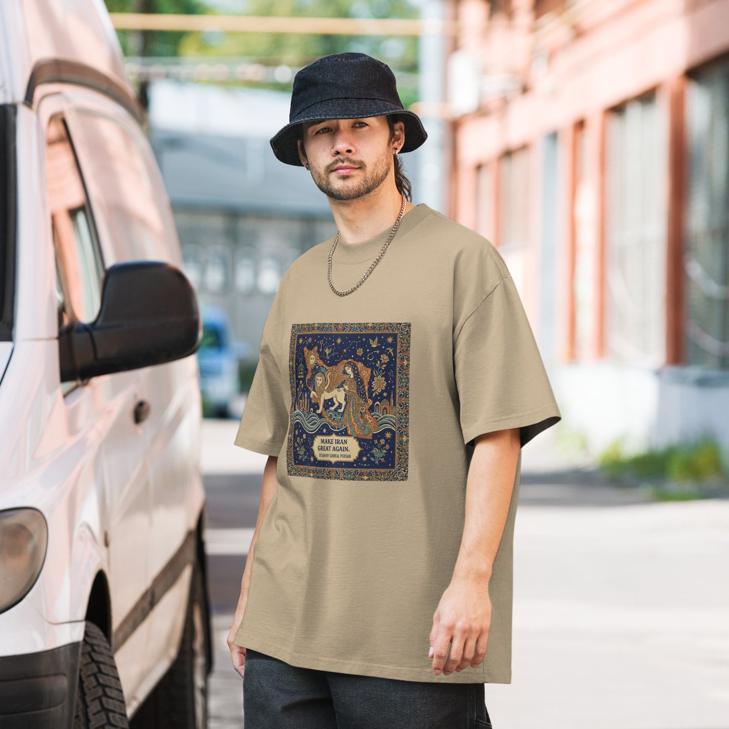 Man wearing a beige t-shirt with a graphic design, standing next to a van.