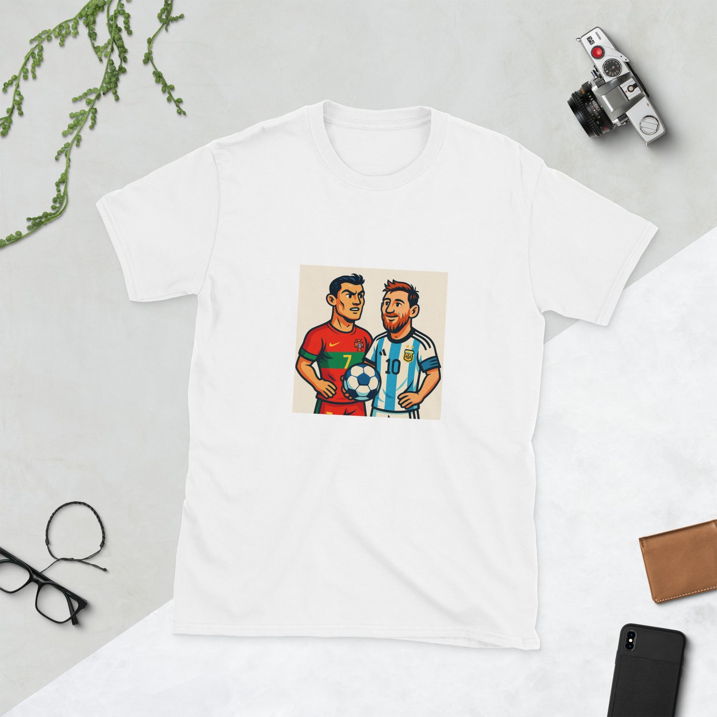 White t-shirt with a graphic of two soccer players on a light gray surface with a phone, wallet, and glasses.