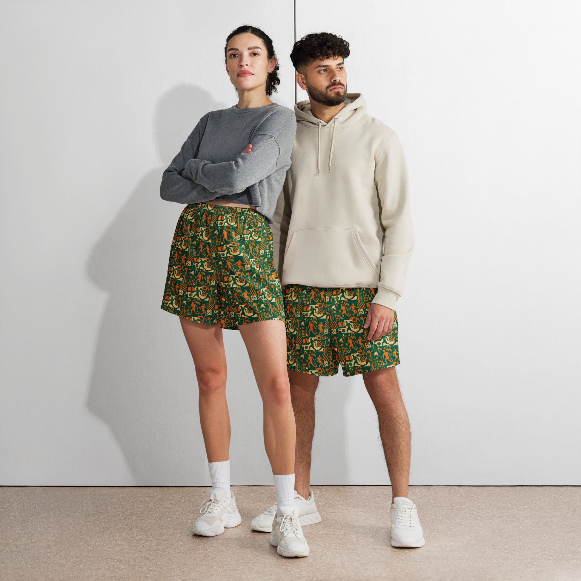 Two people wearing matching green patterned shorts and gray and beige hoodies against a white background.