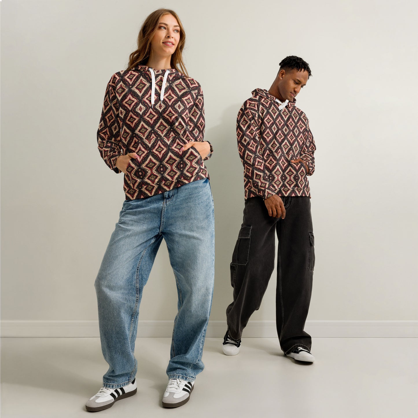Two people wearing patterned hoodies and jeans against a plain background