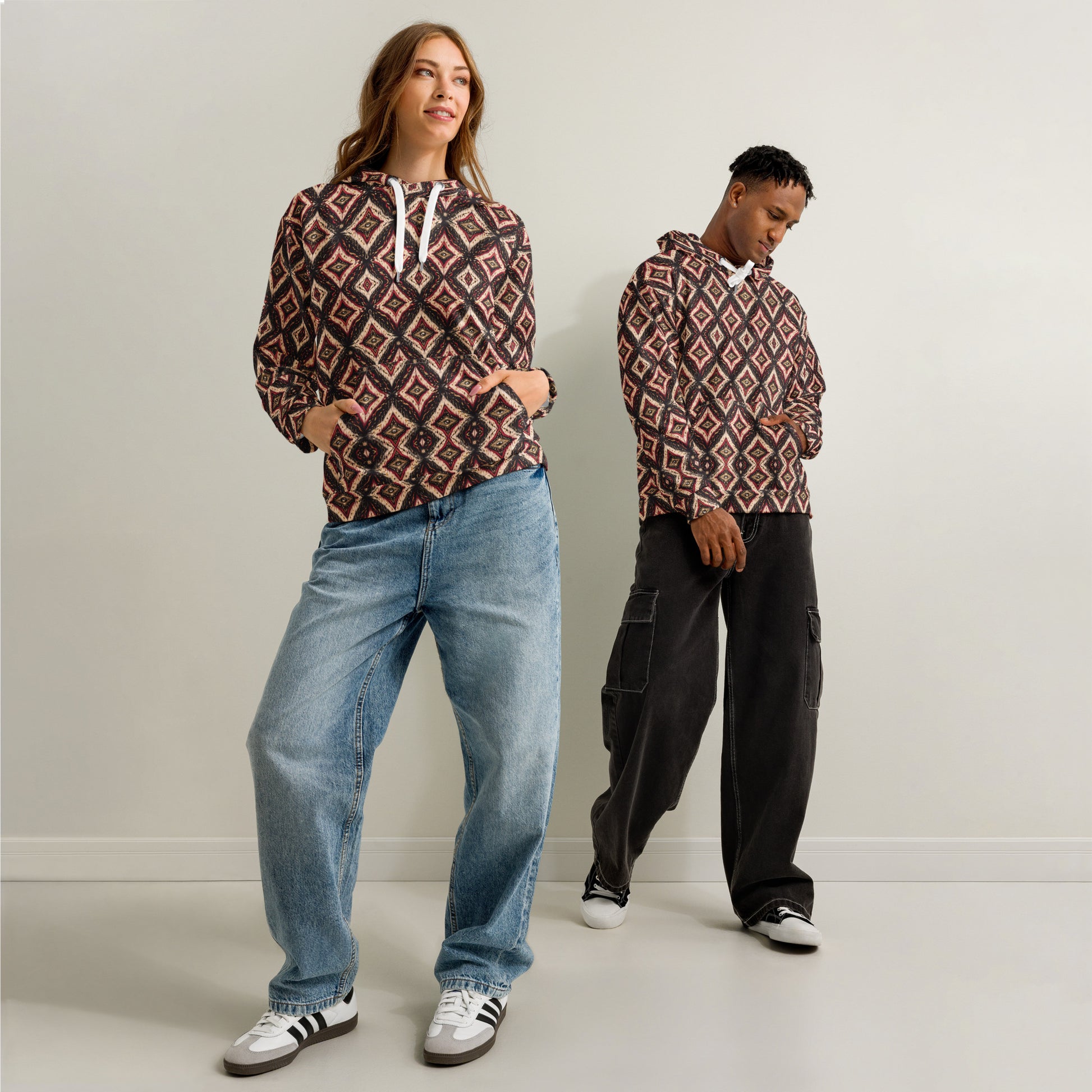 Two people wearing patterned hoodies and jeans against a plain background