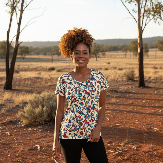 A woman with curly brown hair wearing a short-sleeve crewneck t-shirt with a colorful paisley pattern on a cream background, paired with black pants, against a plain white background.