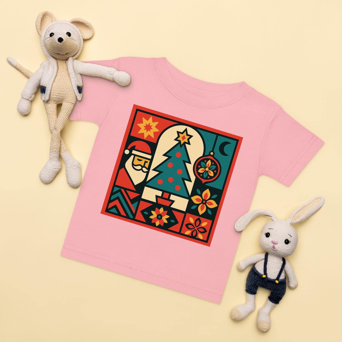 Pink t-shirt with a colorful graphic design, surrounded by two stuffed animals on a light yellow background.