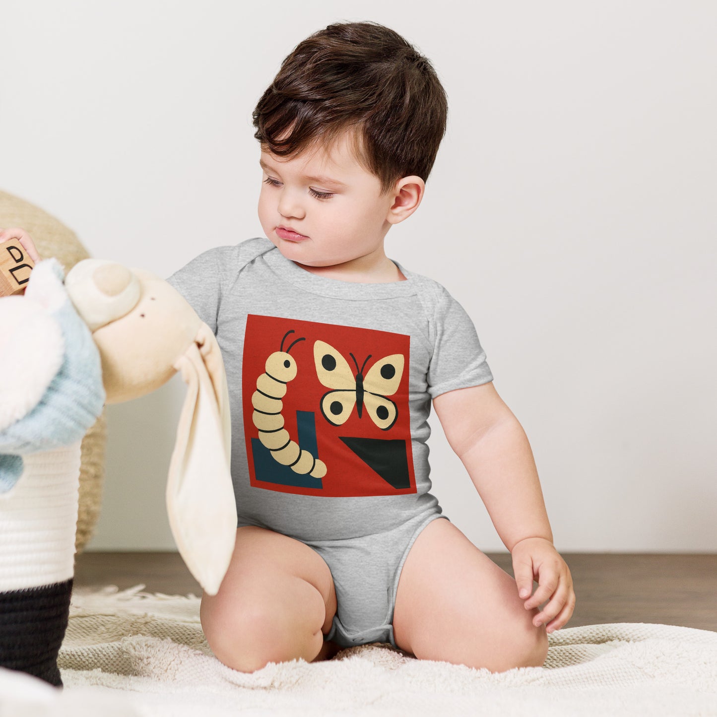 Child wearing a gray onesie with a colorful butterfly design, sitting on a white surface.