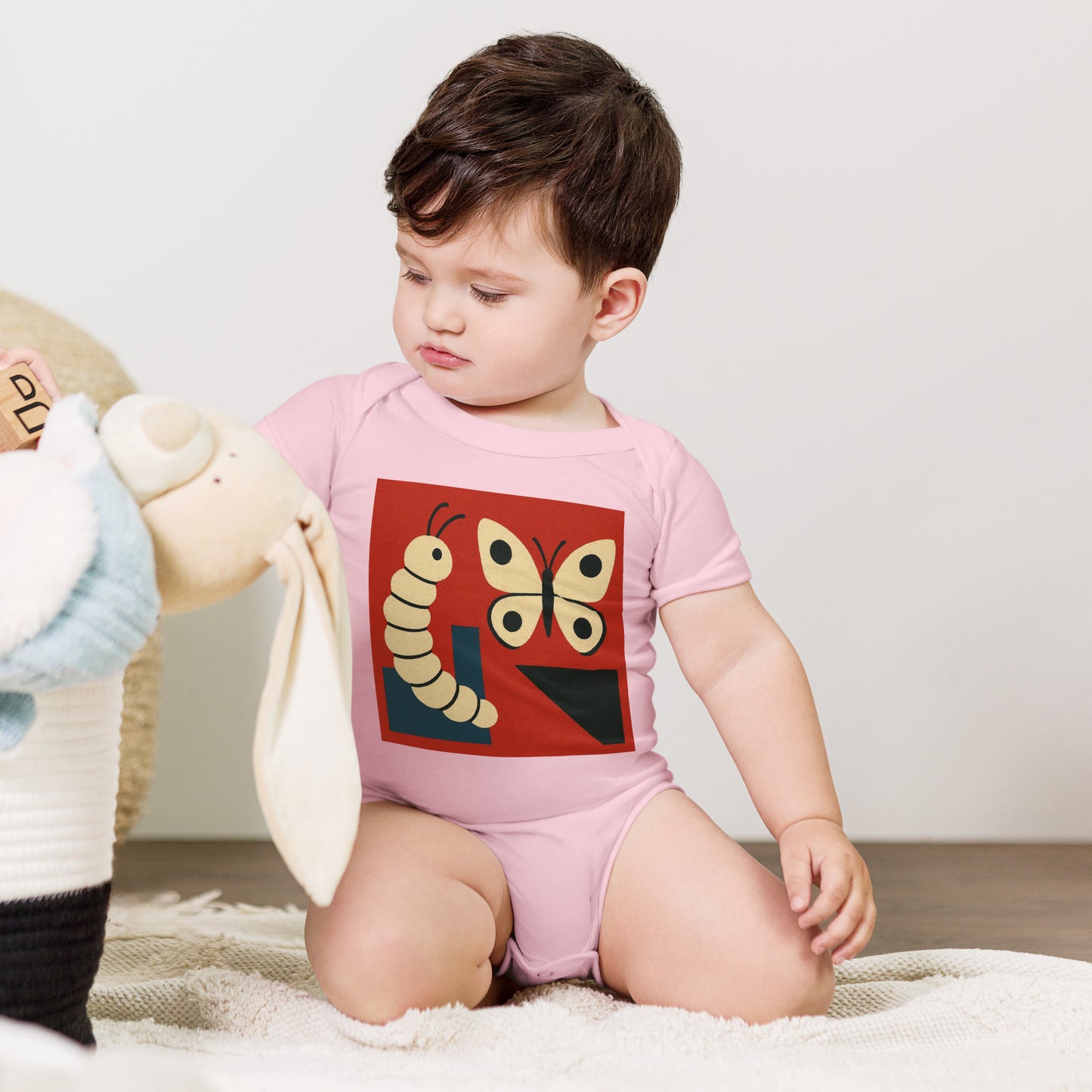 Child wearing a pink onesie with a butterfly design, sitting on a white blanket.