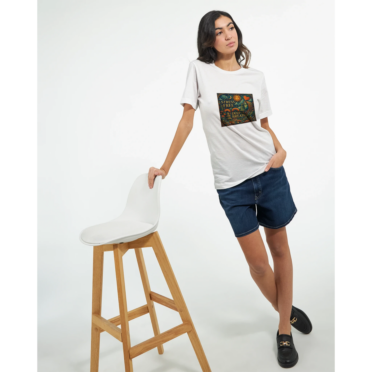 Woman wearing a white t-shirt with a graphic design, standing next to a white stool on a white background