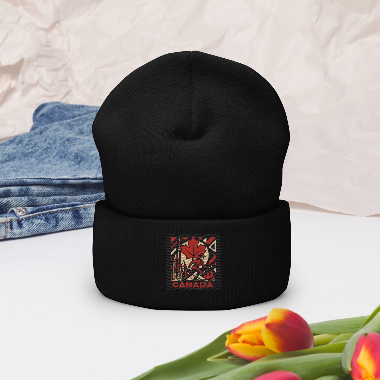 Black beanie with a Canada-themed patch on a white surface with jeans and tulips.