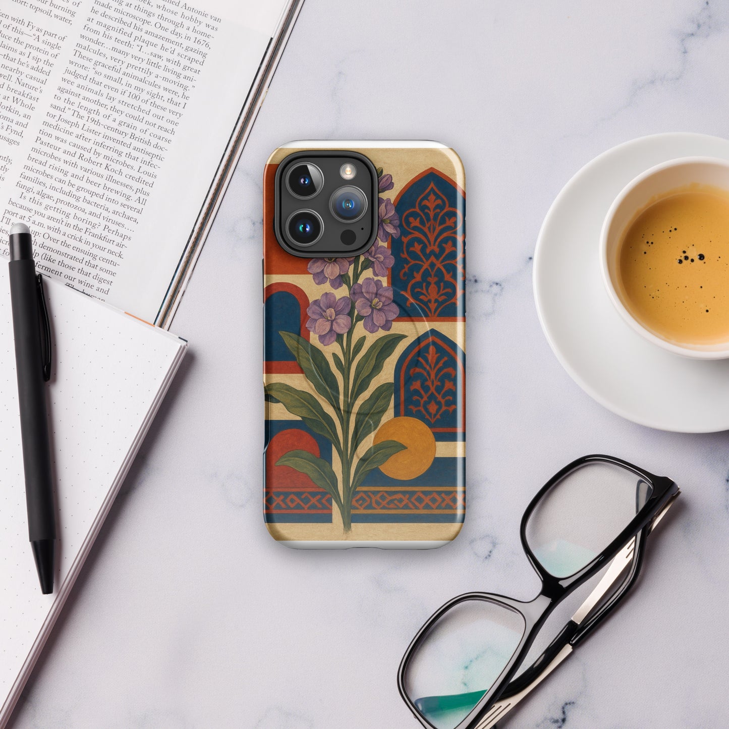 Phone case with floral design on a marble surface with a book, pen, and coffee cup.
