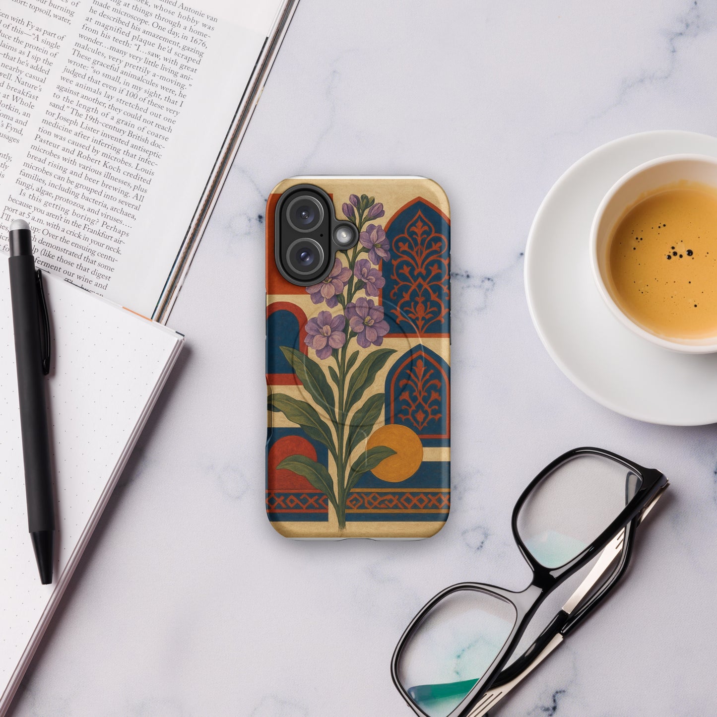 Phone case with floral design on a marble surface with a book, pen, and coffee cup.
